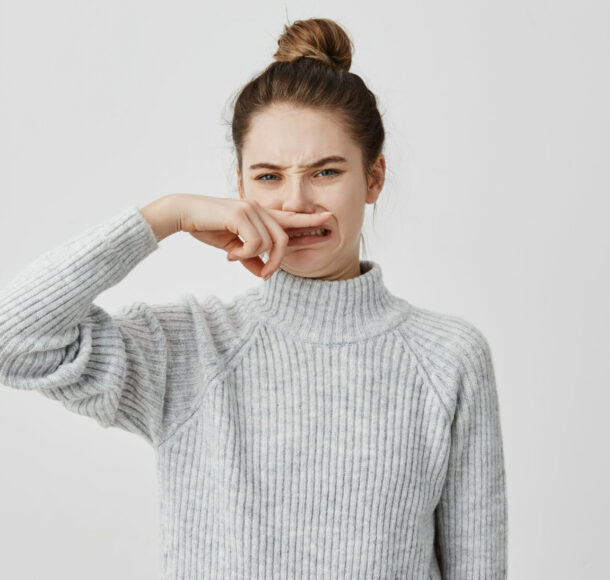 Displeased woman wearing casual closing nose with index finger looking with disgust. Young female blogger smelling something unpleasant while working in cafe. Bad smell concept